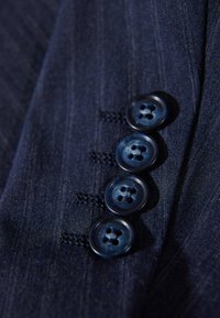 Marinfärgad tyg med en subtil textur har fyra rundade blå knappar, var och en med fyra hål, som är säkert sydda på plats.