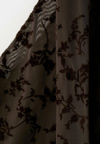 Tissu marron foncé transparent avec des motifs floraux en velours, drapé avec des ombres douces et de la lumière sur un fond en maille texturée.