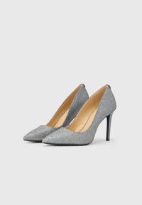 Sudraba mirdzoši augstpapēžu apavi ar izteiksmīgu purngalu un pārslēgtu stiletto papēdi. Gluda iekšējā apdare un minimāla sānu izgriezums, lai parādītu kāju.