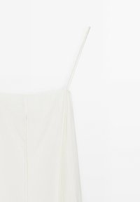 Robe blanche sans manches avec fines bretelles spaghetti et détail de couture verticale à l'avant sur fond uni.
