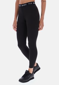 Czarne legginsy sportowe z wysokim, elastycznym pasem w białym kolorze z logo. Gładki materiał, dopasowany krój i długość do kostek. W zestawie z czarnymi sneakersami.