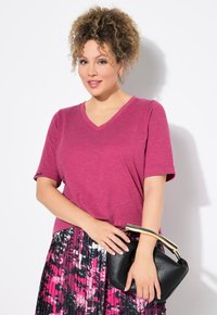 Magenta V-hals T-shirt met korte mouwen, gecombineerd met een zwarte geplooide rok met een roze abstract patroon en een zwarte handtas met een gouden handvat.