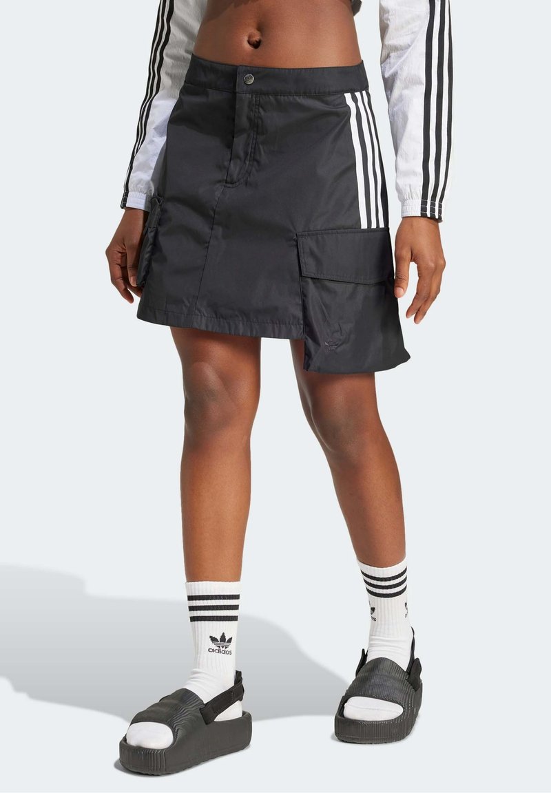 Black nylon cargo skirt with two side pockets and three white stripes, paired with black sandals and white striped socks.