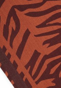 Close-up of a fabric with an abstract dark brown tiger stripe pattern on a burnt orange background.