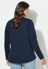 Top a maniche lunghe blu navy con vestibilità rilassata, caratterizzato da spacchi laterali e una texture liscia, abbinato a jeans in denim blu chiaro.
