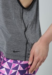 Canotta atletica grigia con cuciture nere e un piccolo logo Nike sull'orlo, abbinata a leggings con un vivace motivo geometrico rosa e viola.