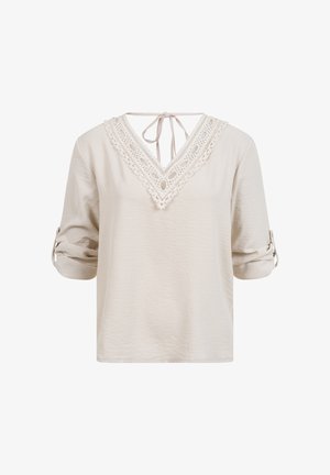 Blouse beige à manches longues avec poignets retroussés, encolure en V en dentelle, et fermeture à nouer dans le dos.