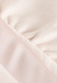 Puha bézs színű kötött anyag, sima, világos rózsaszín szegéllyel. Texturált felület finom mintázattal és lágy eséssel.