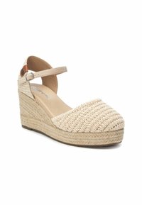 Escarpin compensé beige avec une tige en textile tissé, bout fermé, bride de cheville et une semelle en jute texturée. Présente un petit bouton en accent.