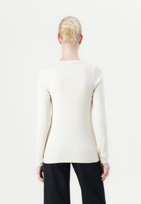 Lange mouwen crème top met een geribbelde textuur, aansluitend ontwerp en een ronde halslijn. Heeft een rechte zoom en subtiele stikdetails.