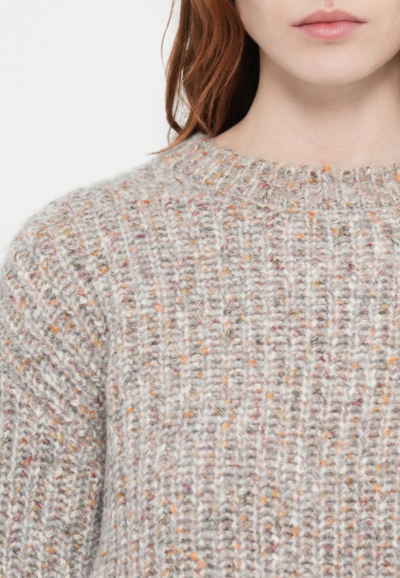 Dikke gebreide trui in lichtgrijs met meerkleurige flekken. Heeft een ronde halslijn en een textuurstof, wat warmte en volumineusheid benadrukt.