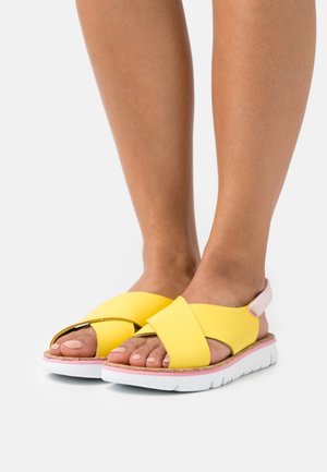 Sandales jaunes à lanières croisées avec une semelle blanche et un accent rose, fabriquées en matériau synthétique avec un design ouvert sur l'avant et un semelle texturée.