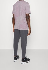 Hellblaues, batikmäßiges T-Shirt mit kurzen Ärmeln, kombiniert mit dunkelgrauen Jogginghosen und schwarzen Sneakers mit weißen Akzenten.