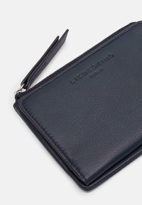 Portefeuille en cuir bleu marine avec une surface texturée et un logo en relief. Il comporte une fermeture éclair et une fente pour cartes avec un petit onglet en cuir.