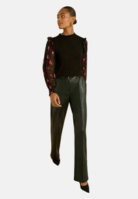 Fekete felső áttetsző, mintás ujjal, rózsaszín részletekkel, magas derekú, szabott fekete bőrnadrággal és hegyes orrú fekete magassarkú cipővel párosítva.