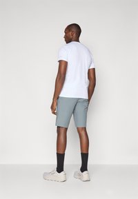 T-shirt à manches courtes gris clair et short gris clair assorti, associés à des baskets grises et des chaussettes noires, vus de dos.