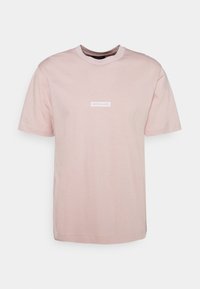 Světle růžové bavlněné tričko s kulatým výstřihem, krátkými rukávy a bílým obdélníkovým logem s textem "Nørgaard" na přední straně.