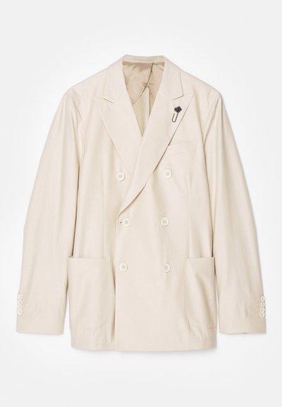 Μπεζ διπλό-ύφαντος σακάκι με γιακά με στόχο, δύο μεγάλες μπροστινές τσέπες και μία μικρή μαύρη καρφίτσα κοντά στον γιακά. Απαλή υφή υφάσματος.