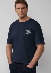 Marineblauwe katoenen t-shirt met korte mouwen, ronde halslijn en witte tekst: "DRIVE STUNT UNIT MOTION PICTURES 9362-309-13" op de borst.