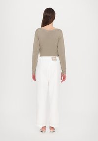 Beige genser med utskåret bak, kombinert med hvite vide bukser. Buksene har elastisk liv og et merke med etiketten "MM".