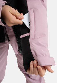 Waterdichte jas van roze en zwarte stof. Voorzien van een veilige binnenzak en verstelbare cuffs voor een goede pasvorm. Textuur oppervlak.