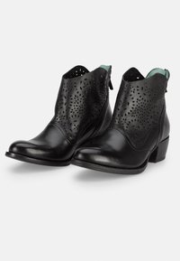 Botas de piel negra hasta el tobillo con perforaciones recortadas, punteras redondeadas y pequeños tacones apilados. Acentuadas con un forro interior en contraste.
