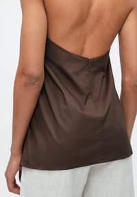 Καφέ αμάνικη μπλούζα με χαμηλή πλάτη, διαθέτει κεντρική ραφή και διακριτικό φερμουάρ. Κατασκευασμένη από λεία, ελαφριά ύφανση.