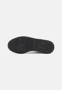Semelle de chaussure en caoutchouc noir avec un motif de grip texturé et un logo, présentant un accent circulaire et des bords lisses pour un soutien structuré.