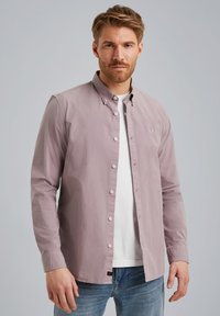 Camicia a maniche lunghe di colore viola chiaro, con colletto, abbinata a una maglietta bianca e jeans di denim. Presenta bottoni bianchi e dettagli del logo.