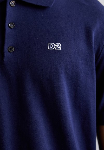 Tamsiai mėlynas polo marškinėliai, pagaminti iš tekstūrinio audinio, su dviem mygtukais priekyje ir balta siuvinėta "D2" logotipu ant krūtinės.