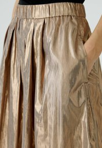 Metaalachtige bronzen geplooide rok met een gestructureerde afwerking, elastische tailleband en zijzakken. Licht weerkaatst op de gladde stof.