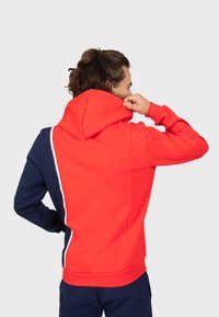 Felpa con cappuccio rossa e blu navy con una striscia bianca accentata dalla spalla al fianco. Tessuto morbido con una texture liscia, tasche a marsupio.