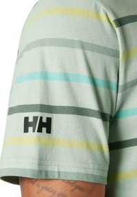 Camiseta de manga corta verde claro con rayas horizontales en gris, amarillo y teal. Logo negro "HH" en la manga izquierda. Textura de tela suave.