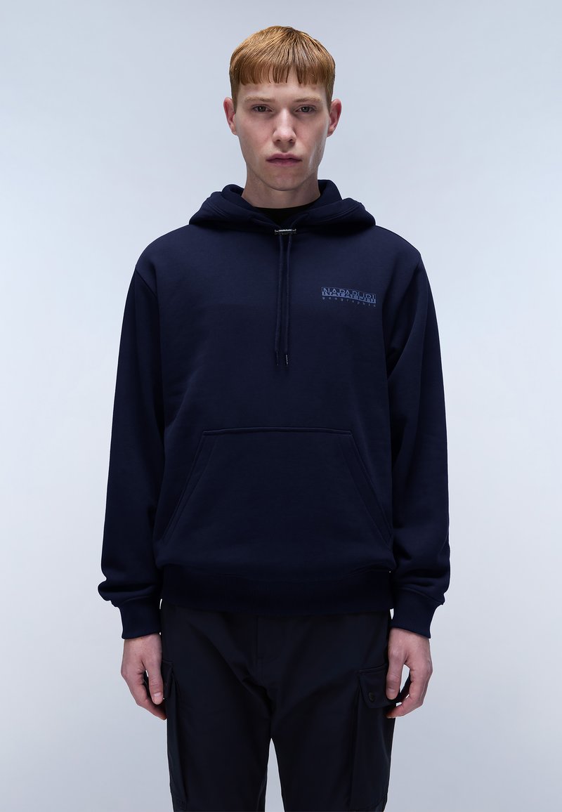 Marineblauwe hoodie met een zak aan de voorkant, een trekkoord kap, zachte stof en geborduurd logo op de borst. Model staat tegen een lichte achtergrond.