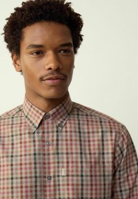 Camicia con bottoni caratterizzata da un motivo a quadri multicolore in tonalità di rosso, verde e neutri, con colletto appuntito e bottoni blu.