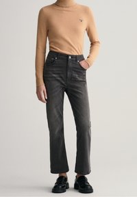 Jersey de cuello alto color beige, de corte ajustado, combinado con jeans oscuros de tiro alto en gris. Diseño de pierna recta con bolsillos, acabado texturizado, usado con zapatos negros.