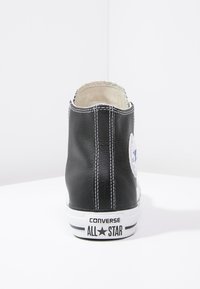 Baskets montantes en cuir noir avec accents blancs, logo signature sur le côté et surpiqûres contrastantes à l'arrière. Semelle en caoutchouc visible en dessous.