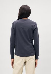 Langarm, donkergrijze katoenen shirt met een ronde halslijn en een iets gebogen zoom. Eenvoudig ontwerp zonder zichtbare patronen of accenten.