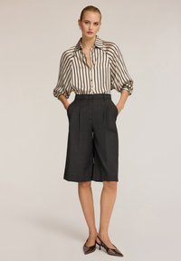 Camicia a righe bianco e nero con maniche arrotolate, abbinata a culotte grigie su misura e tacchi neri lucidi.