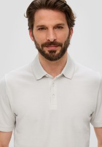 Hellgraues Poloshirt aus strukturiertem Stoff, mit einer Knopfleiste mit drei Knöpfen und einem klassischen Kragen. Schlank geschnitten mit kurzen Ärmeln.