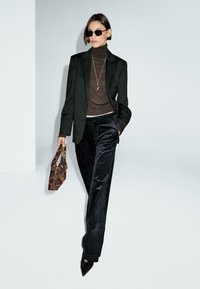 Blazer nero su misura, dolcevita marrone, pantaloni in velluto nero, décolleté neri a punta e borsa in stampa serpente. Gli occhiali da sole completano il look.
