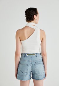 White one-shoulder top paired with blue denim shorts featuring raw hems, back pockets, and green accent on the waistband.