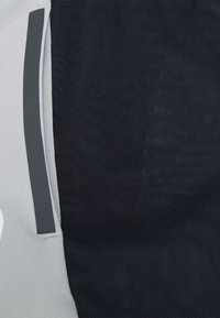 Grå och svart tyg med ett nätliknande mönster, med en kontrasterande slät grå panel och reflekterande detaljer. Ingen synlig logotyp.