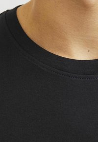 Sort bomulds t-shirt med rund halsudskæring. Næranseende af kraven, der har en glat overflade og tætsiddende syninger langs kanten.