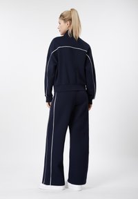 Ensemble sweat-shirt bleu marine et pantalon à jambes larges, avec des détails en passepoil blanc. Confectionné dans un tissu doux, avec une coupe décontractée et un col montant.