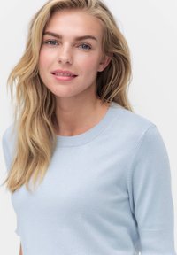 Jasnoniebieski sweter z dzianiny z okrągłym dekoltem i krótkimi rękawami. Materiał wydaje się miękki, o gładkiej teksturze i delikatnym prążkowaniu u dołu.