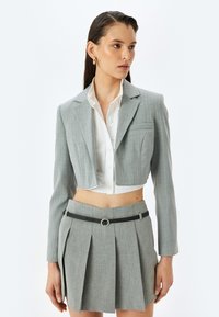 Grijs gestreepte cropped blazer met een notch-kraag, gecombineerd met een witte blouse en een bijpassende geplooide rok met een zwarte gespsluiting.