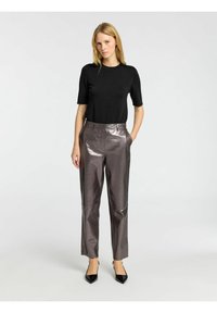 Lyhytnyhtinen musta pusero on yhdistetty metallinvärisiin, korkeavyötäröisiin housuihin. Housuissa on sivutaskut ja kiiltävä pinta. Mustat korkokengät korostavat asua.