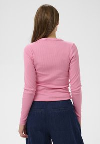 Világos rózsaszín hosszú ujjú bordázott felső. Testhezálló szabású, kerek nyakkivágással. Magas derekú sötétkék farmernadrággal, hátsó zsebekkel párosítva.