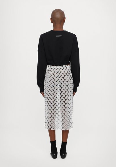 Black cropped sweatshirt with wide sleeves paired with a sheer white skirt featuring a repeating crescent moon pattern. Black ankle socks and shoes.